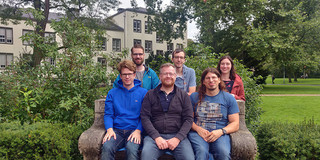 A group of smiling researchers on and behind a stone bench