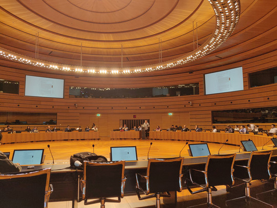 View into a plenary hall at the European Convention Center Luxembourg. Tables with microphones and chairs arrange in a large circle.