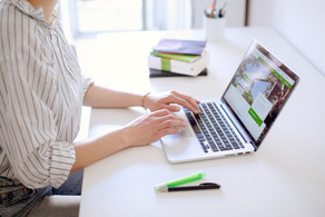 Studentin tippend am Laptop, daneben liegen Bücher und Stifte.